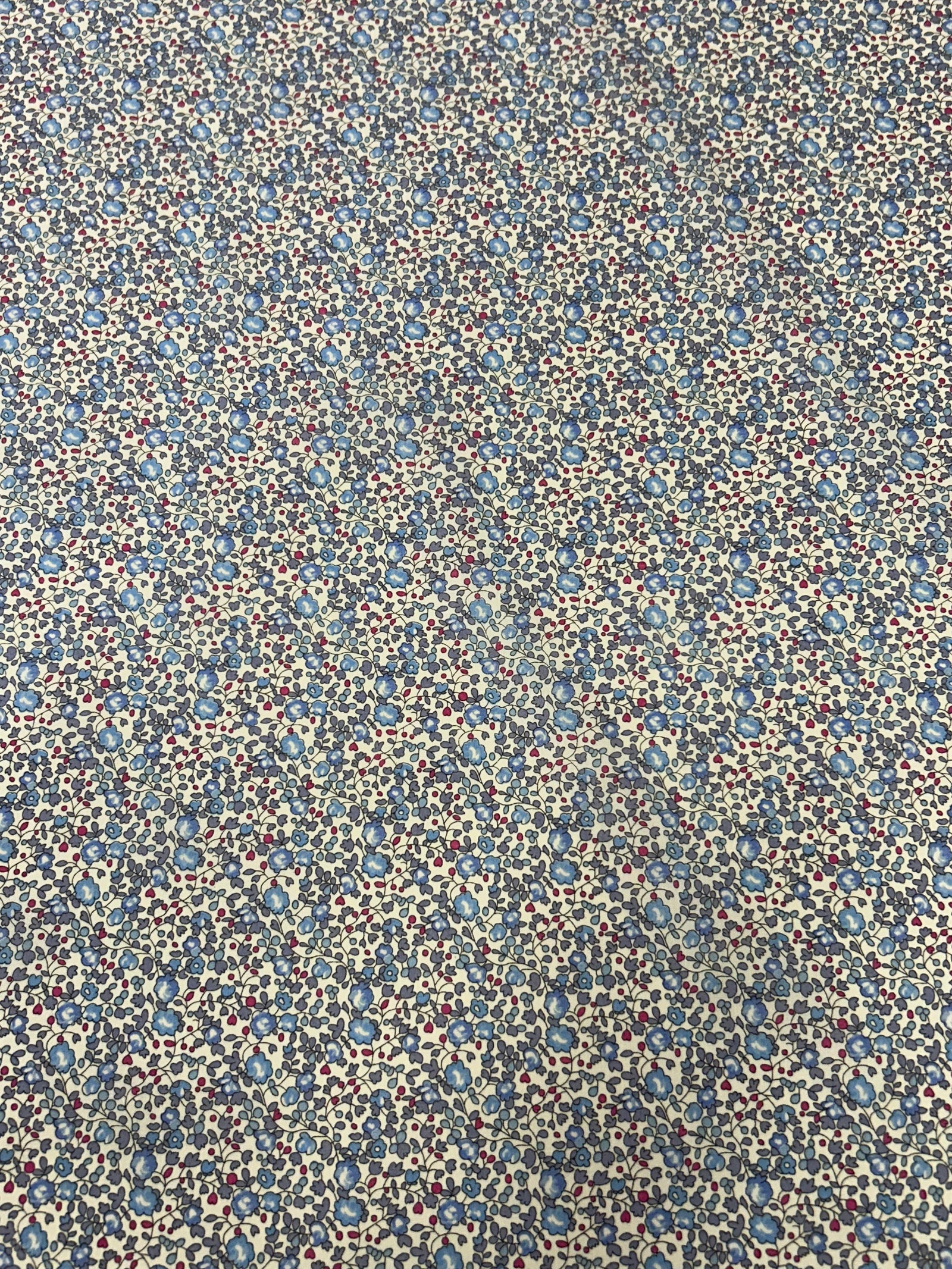  vintage ditsy floral cotton print with dainty blue round flowers with red buds on a white background with a white measuring tape.