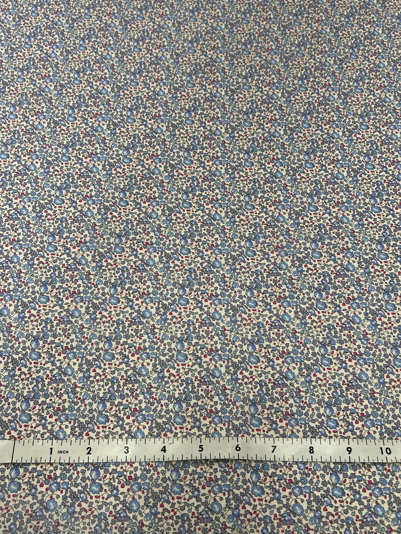  vintage ditsy floral cotton print with dainty blue round flowers with red buds on a white background with a white measuring tape.