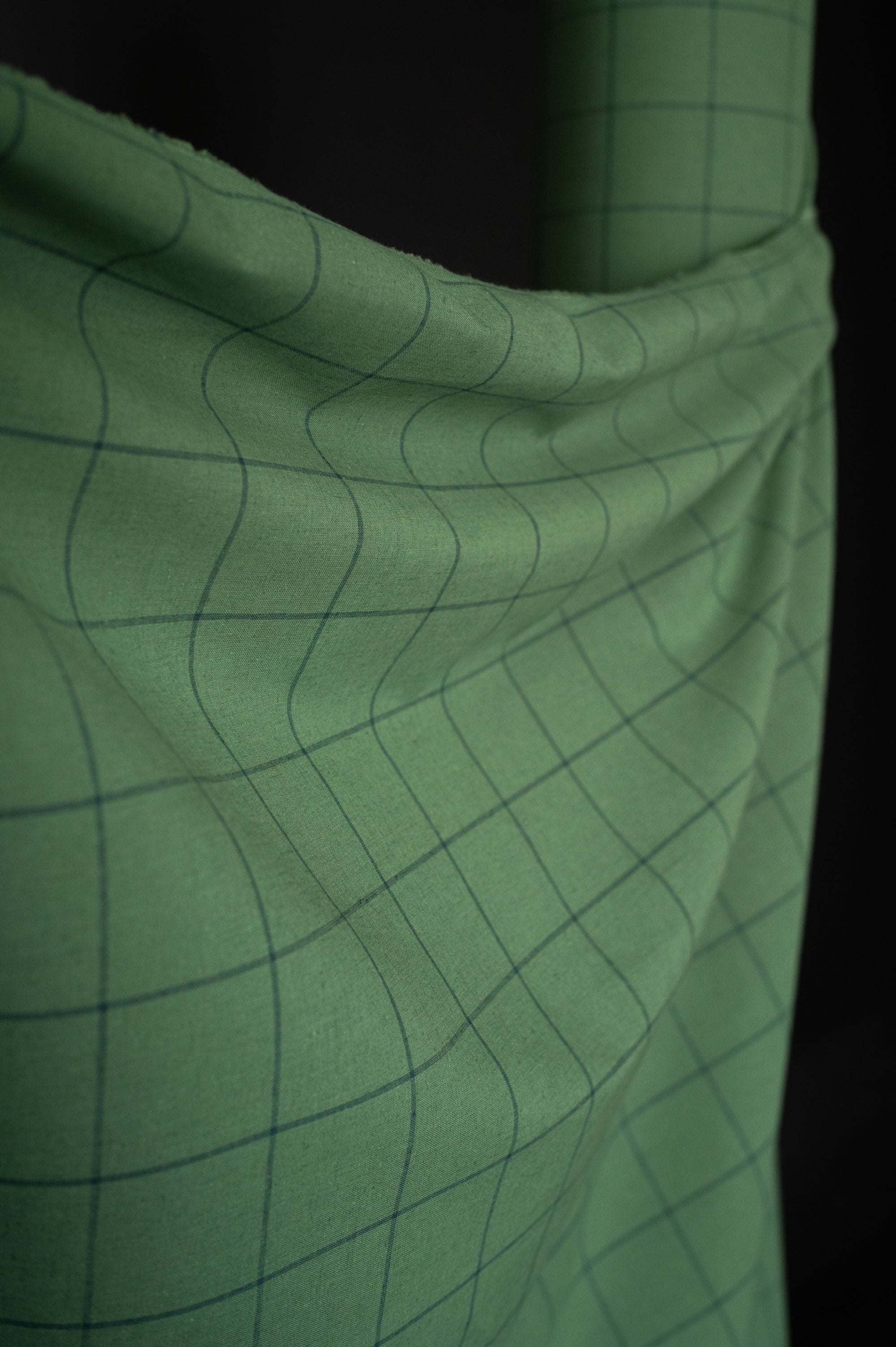 cotton linen fabric in a meadow green with grey blue checks, on a dark grey background.