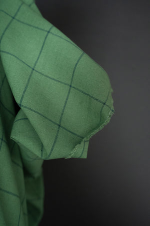 close up cotton linen fabric in a meadow green with grey blue checks, on a dark grey background.