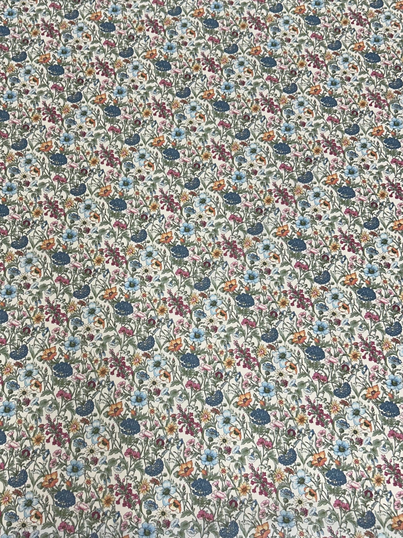 vintage floral Cotton summer garden print with small botanical flowers of blues oranges and purples, nestled among lush green foliage on a white background.