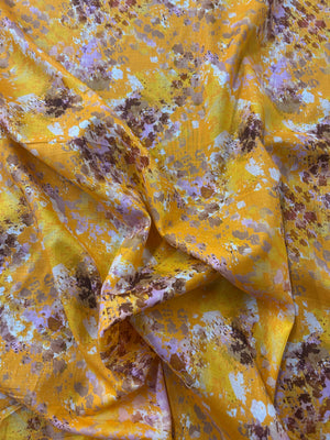 Yellow fabric with watercolor splashes in brown, purple, and white.