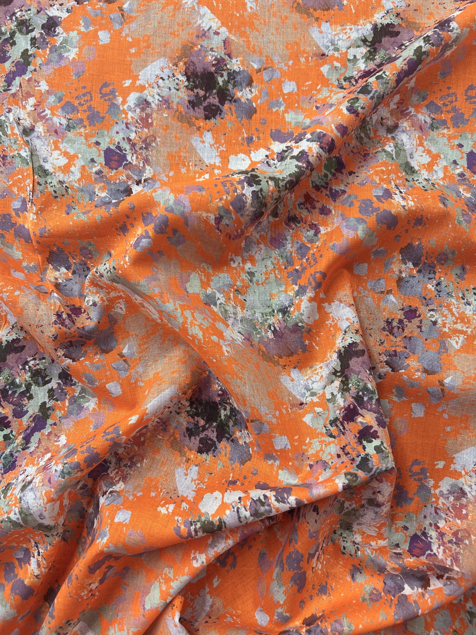 Orange fabric with watercolor splashes in brown, purple, and white.