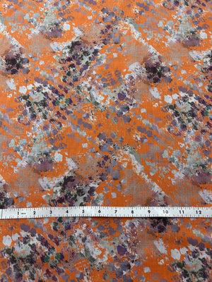 Orange fabric with watercolor splashes in brown, purple, and white.