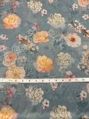 Floral fabric pattern with a pale blue background and large peonies in white and peach with a ruler for scale on a gray background