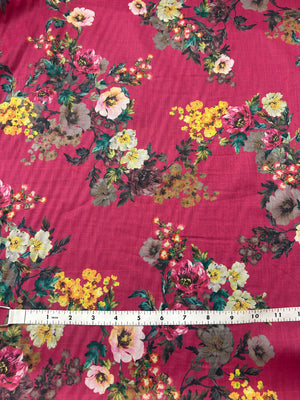 Cotton voile fabric with a vibrant and unsaturated floral print with white, burgundy and yellow flowers on a maroon background with a measuring tape on a red background