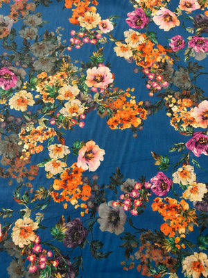 This is a cotton voile with a vibrant and unsaturated floral print of orange, pink and yellow flowers on blue background.