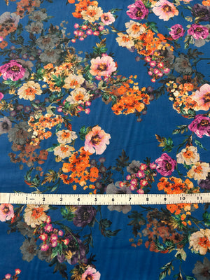 This is a cotton voile with a vibrant and unsaturated floral print of orange, pink and yellow flowers on blue background. with a ruler for scale on a blue background