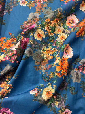 This is a cotton voile with a vibrant and unsaturated floral print of orange, pink and yellow flowers on blue background.