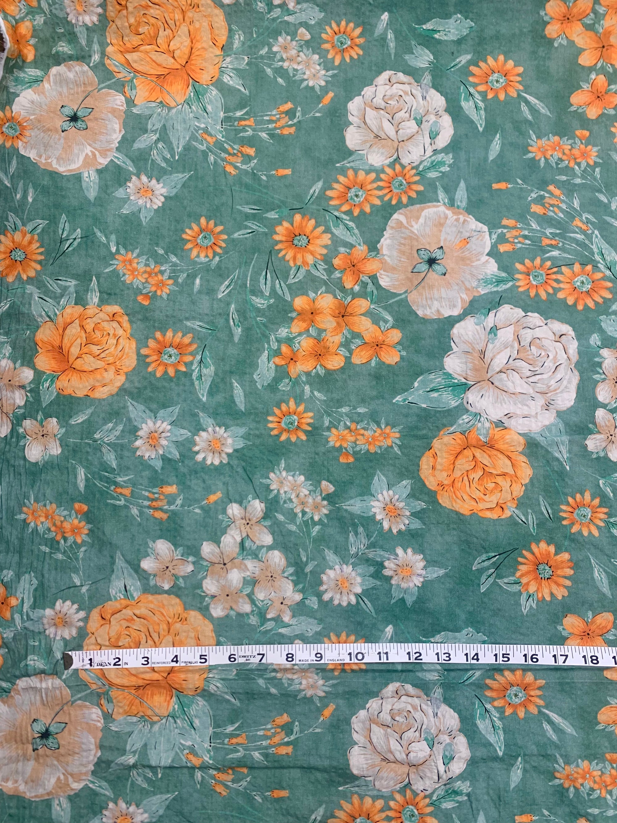 close up of flat cotton seersucker with a muted green, orange and white floral print