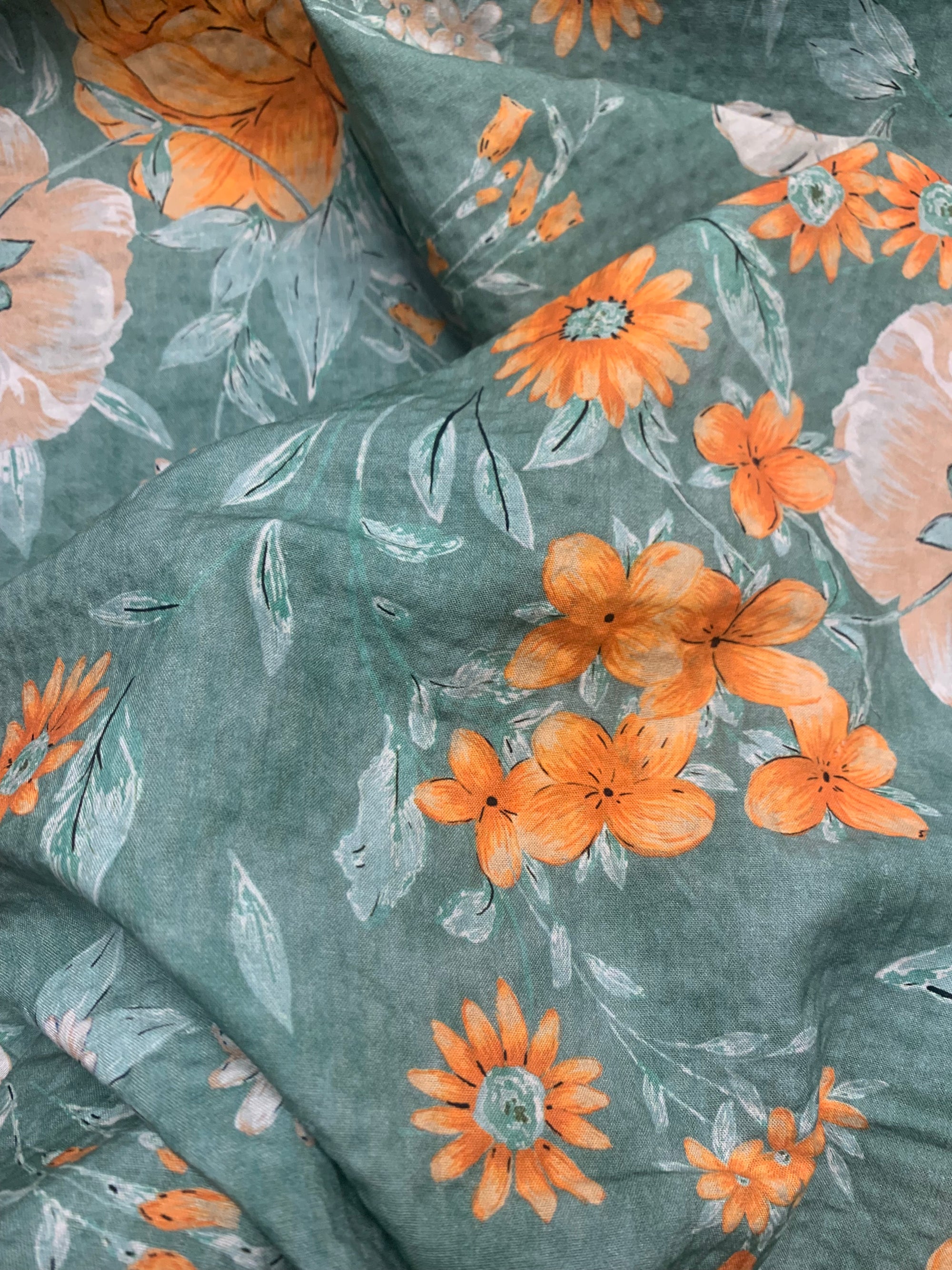 close up of flat cotton seersucker with a muted green, orange and white floral print