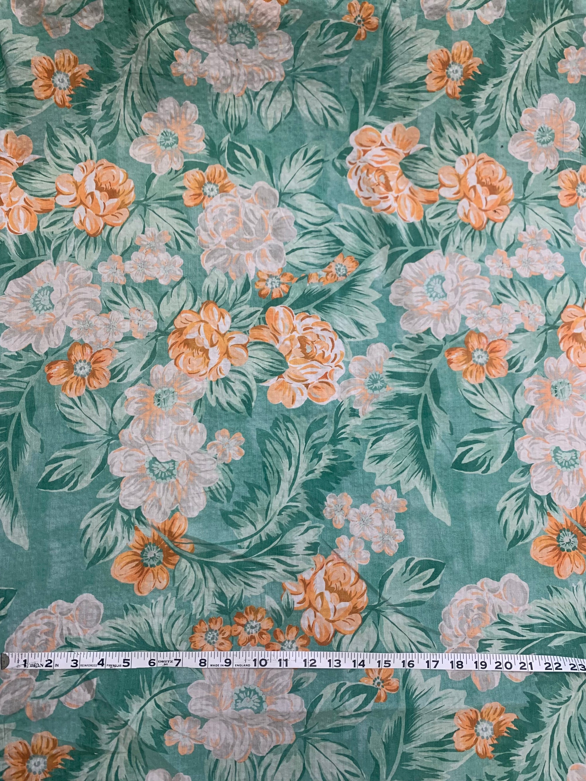 A summery flat cotton seersucker with a muted orange and green tropical print fabric with a measuring tape on top.