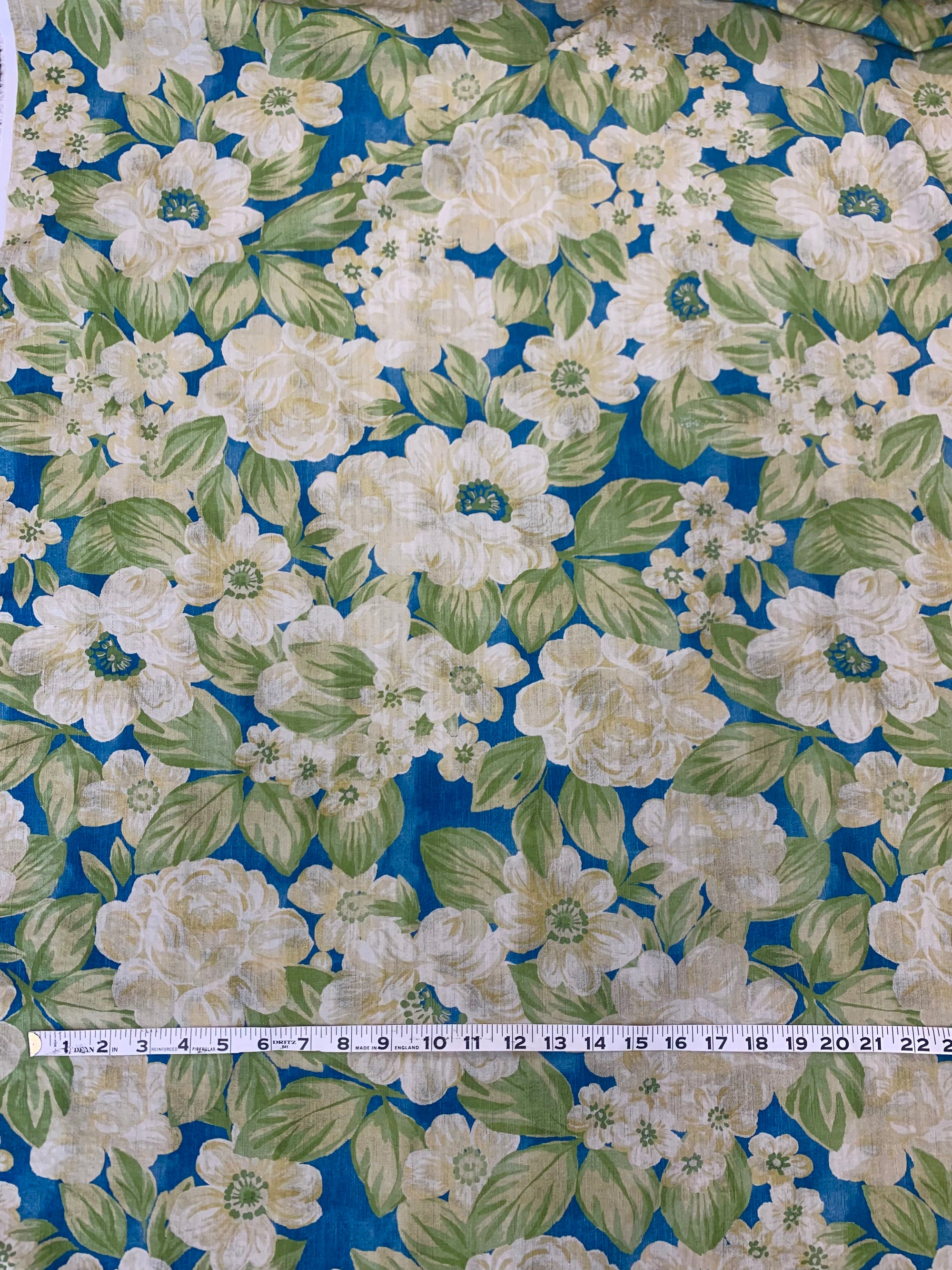 flat cotton seersucker in a royal blue with a beige and green rose floral print with a measuring tape on top.