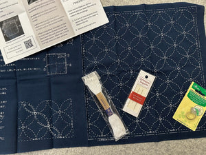 Navy blue fabric with white stitching patterns, a book, and sewing tools on a gray surface.