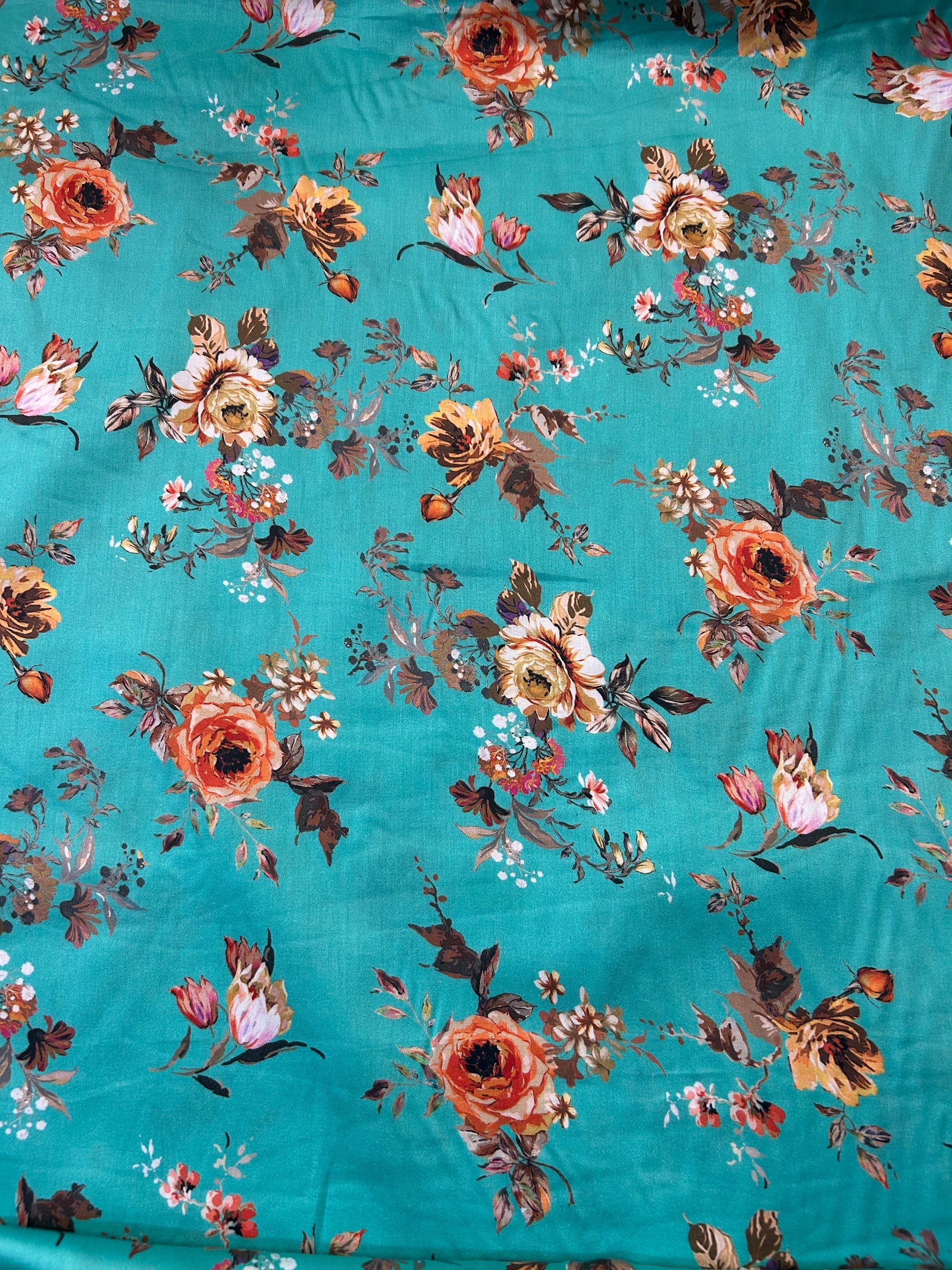 A close-up of a teal fabric with an all-over floral print featuring orange, pink, and brown flowers with green and brown leaves.
