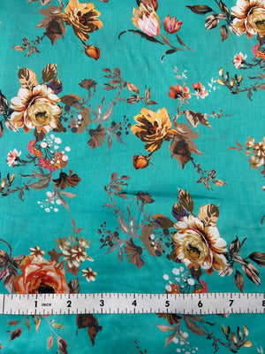 A close-up of teal fabric with a vintage floral print in beige, brown, and muted pink, shown with a white ruler on top for scale.