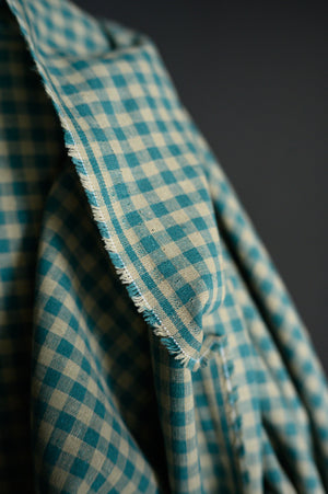 Close up of Teal and tan gingham, cotton/linen blend on a dark grey background.