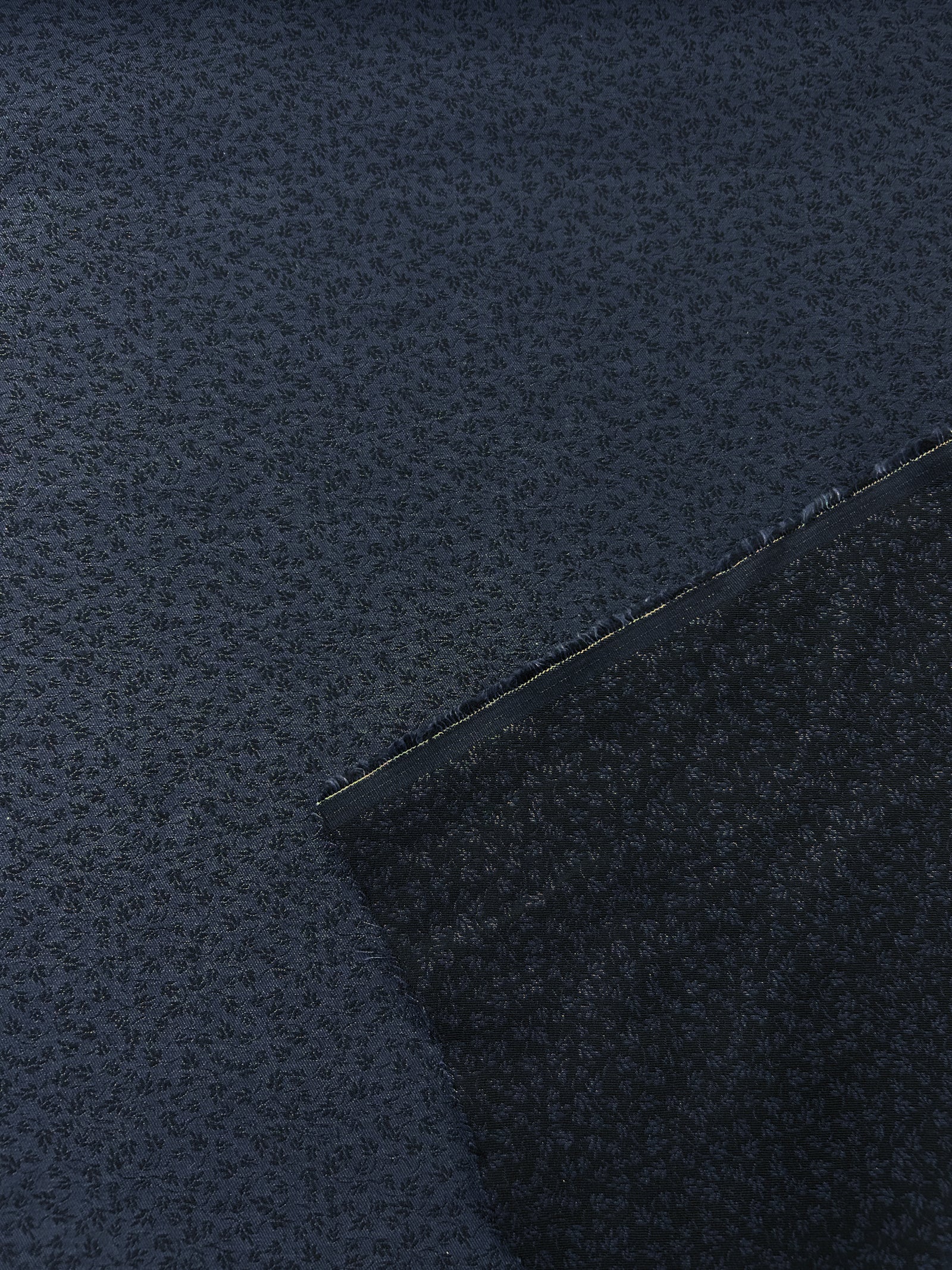 A beautiful light-weight wool/cotton jacquard. Woven with small black flowers on a background of navy blue. With a measuring tape on top.