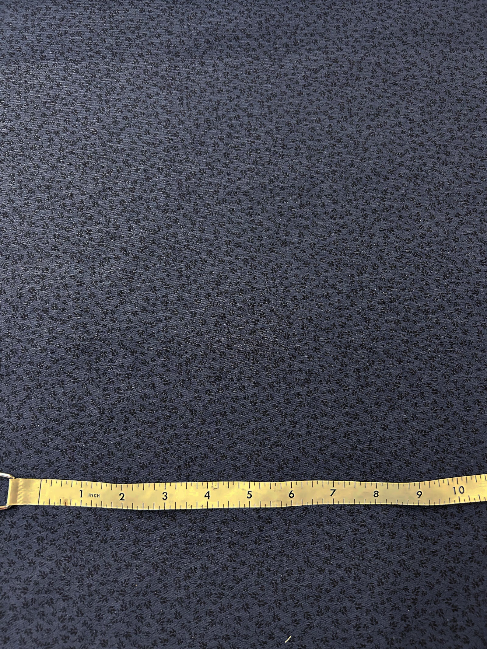 A beautiful light-weight wool/cotton jacquard. Woven with small black flowers on a background of navy blue. With a measuring tape on top.