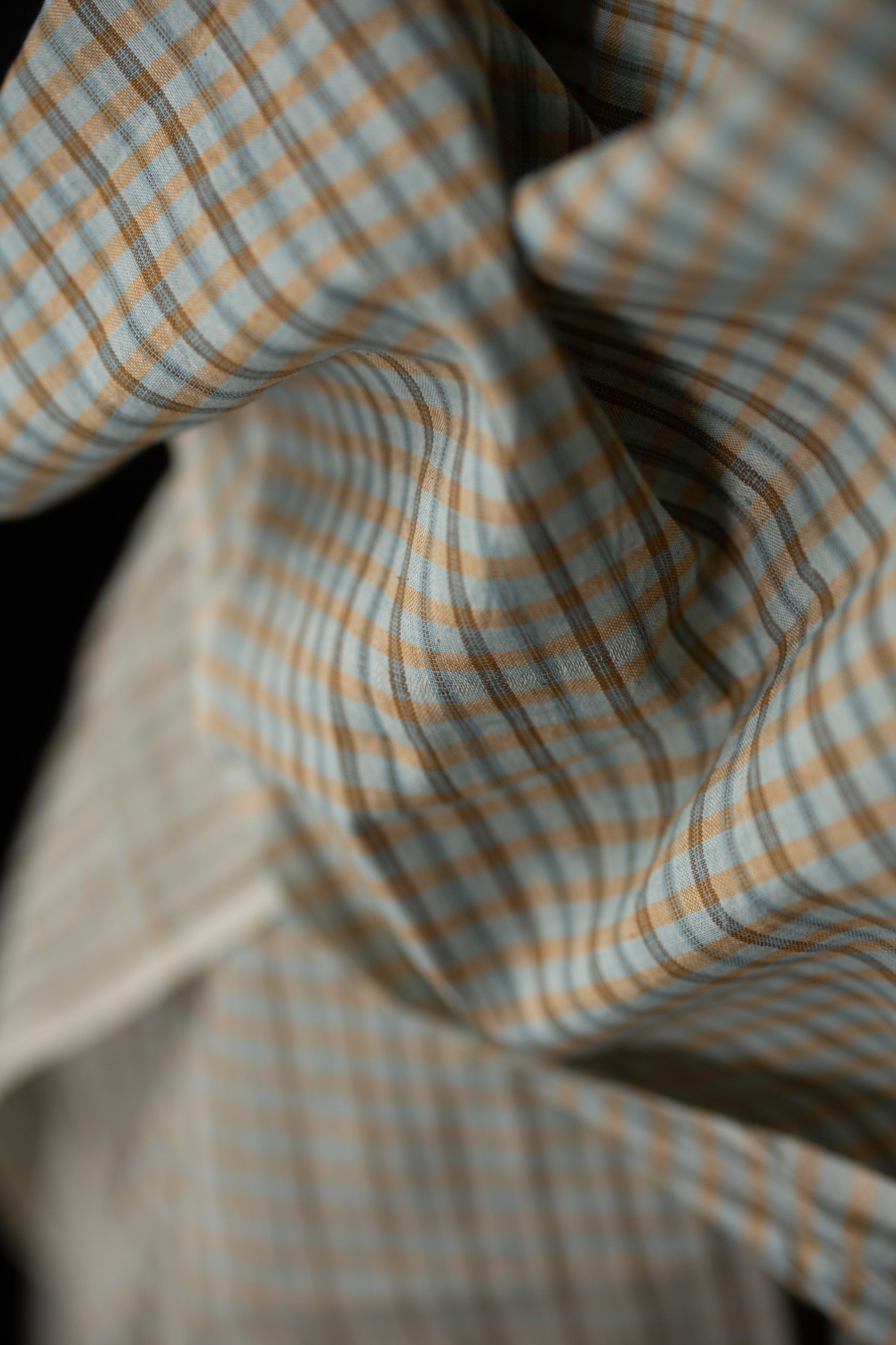 Fabric in a pale blue and pale orange plaid with a very dark grey background.