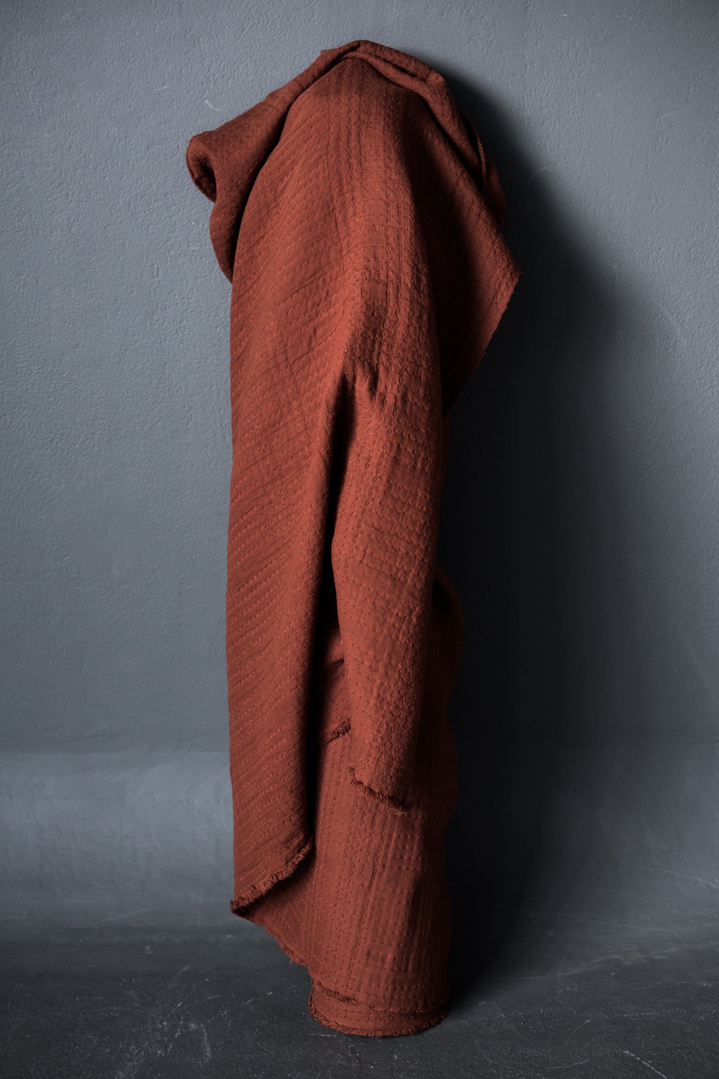roll of deep rust jacquard fabric standing up with a dark grey background.