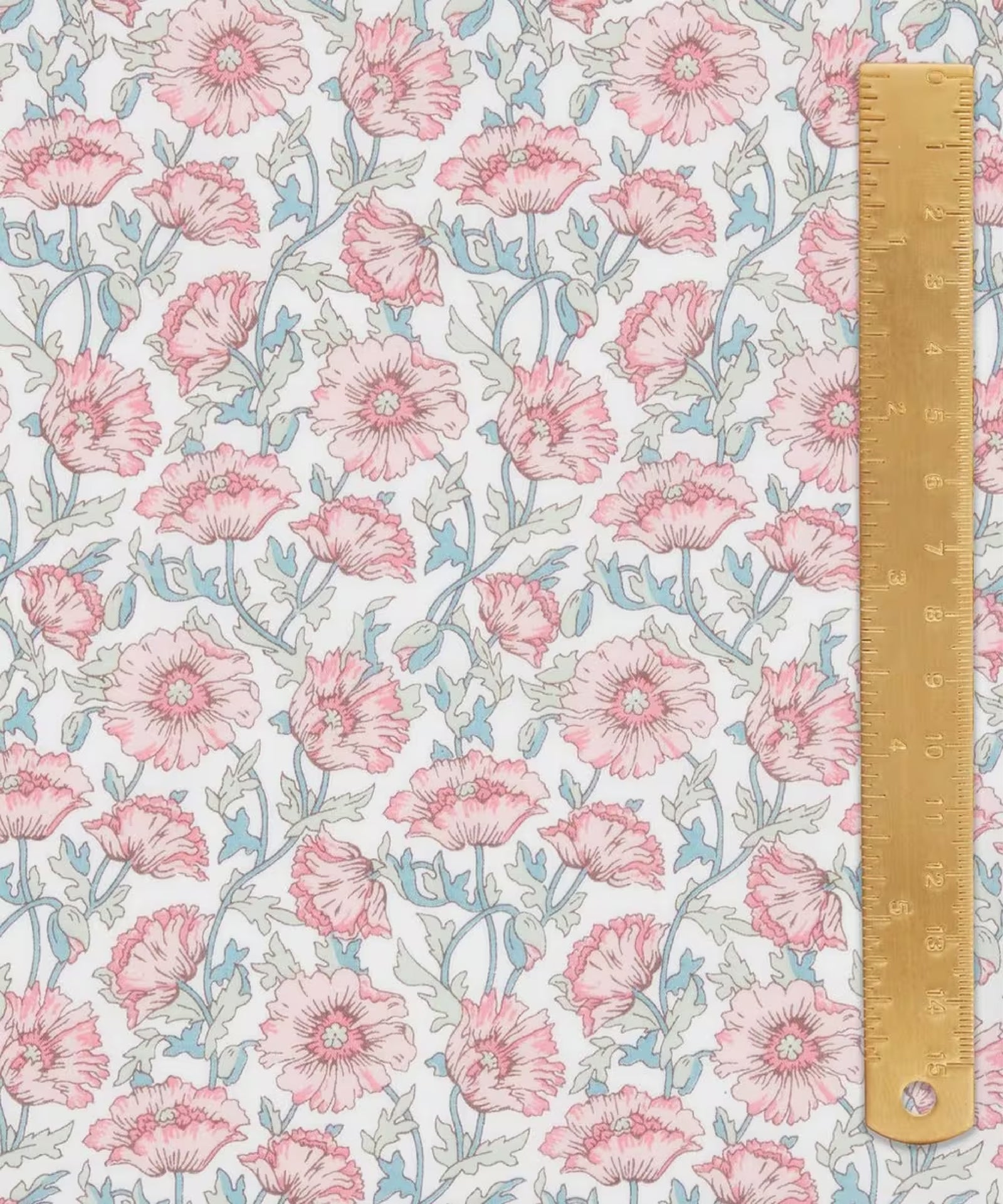 Liberty of London cotton tana lawn in  a beautiful, vibrant print of pink poppies with blue stems on a white background. With a light brown ruler on top.