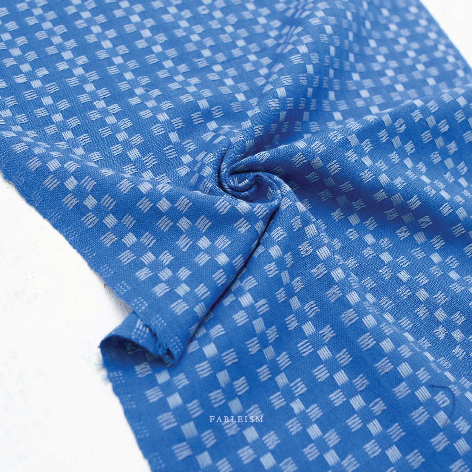 a 100% cotton fabric in a beautiful stunning bright blue color with pale blue woven textured checkered pattern.