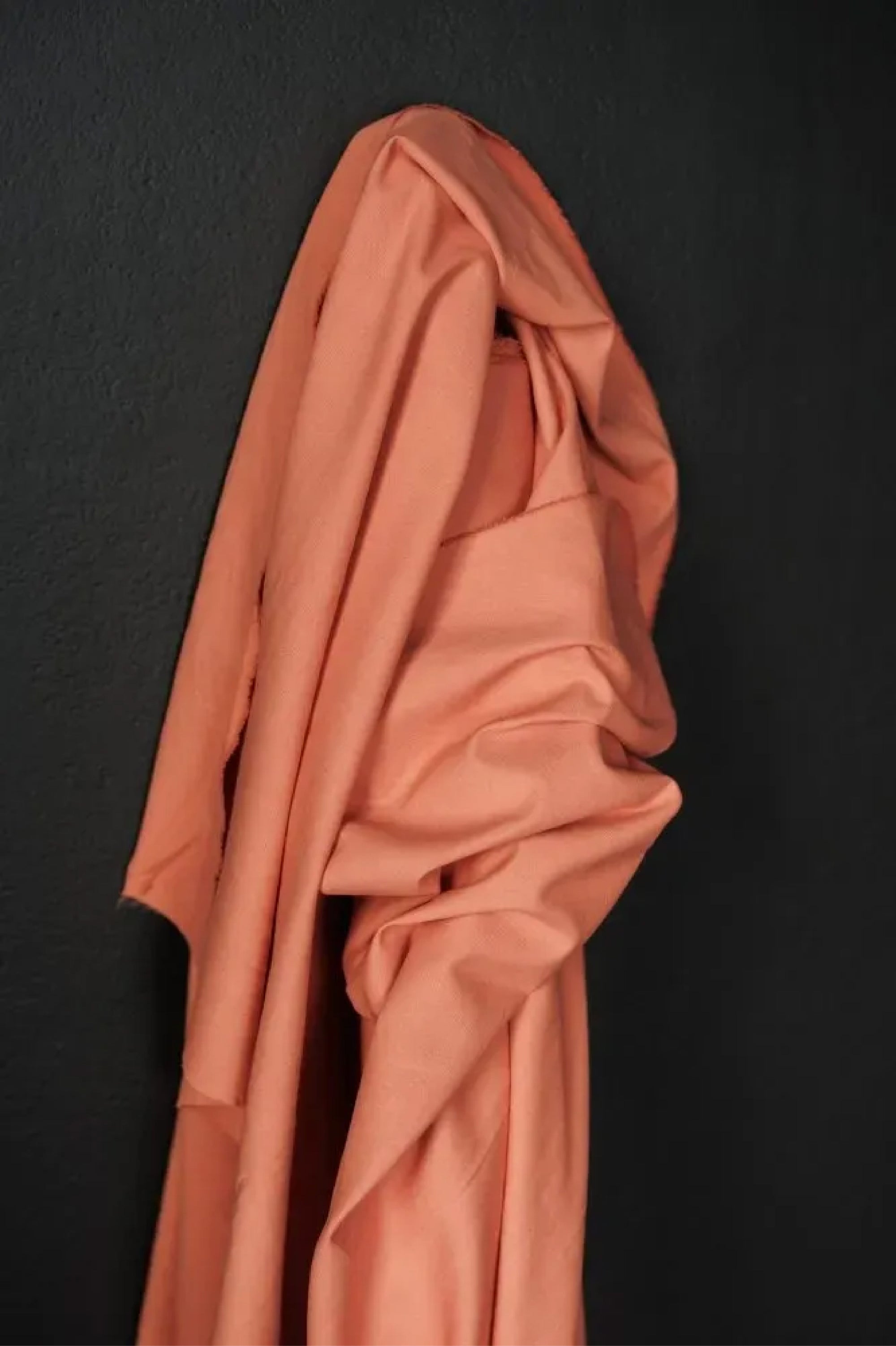 Soft cotton canvas fabric in a coral color on a dark grey background. 