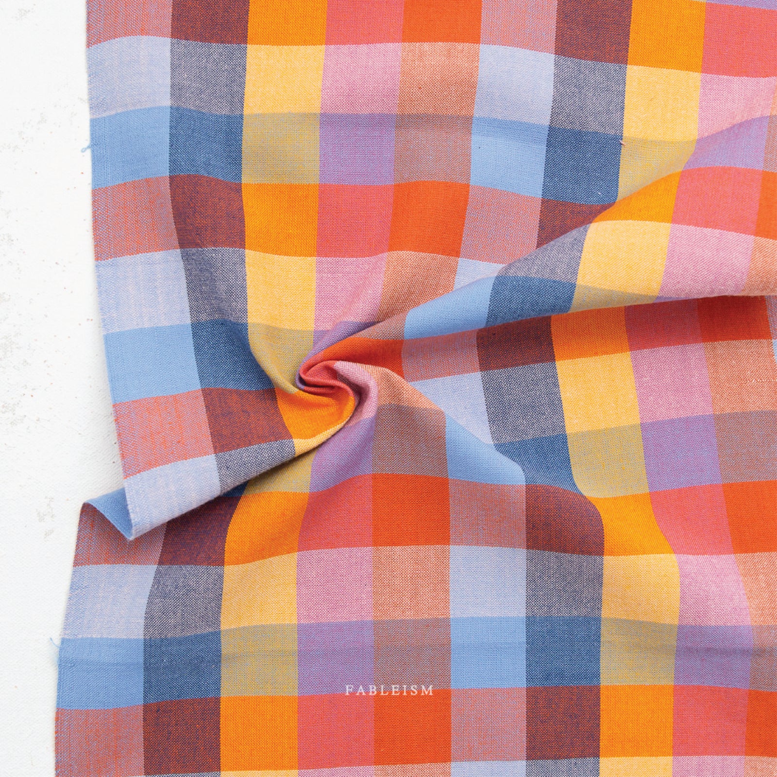 A colorful100% cotton fabric in a bold, woven check pattern in warm oranges, corals, yellows, soft pinks, and cool blues, on a white background.