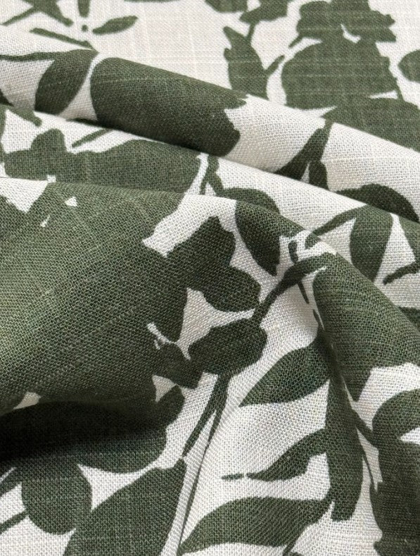 Close up of Italian linen with a green print of floral silhouettes on a white background.