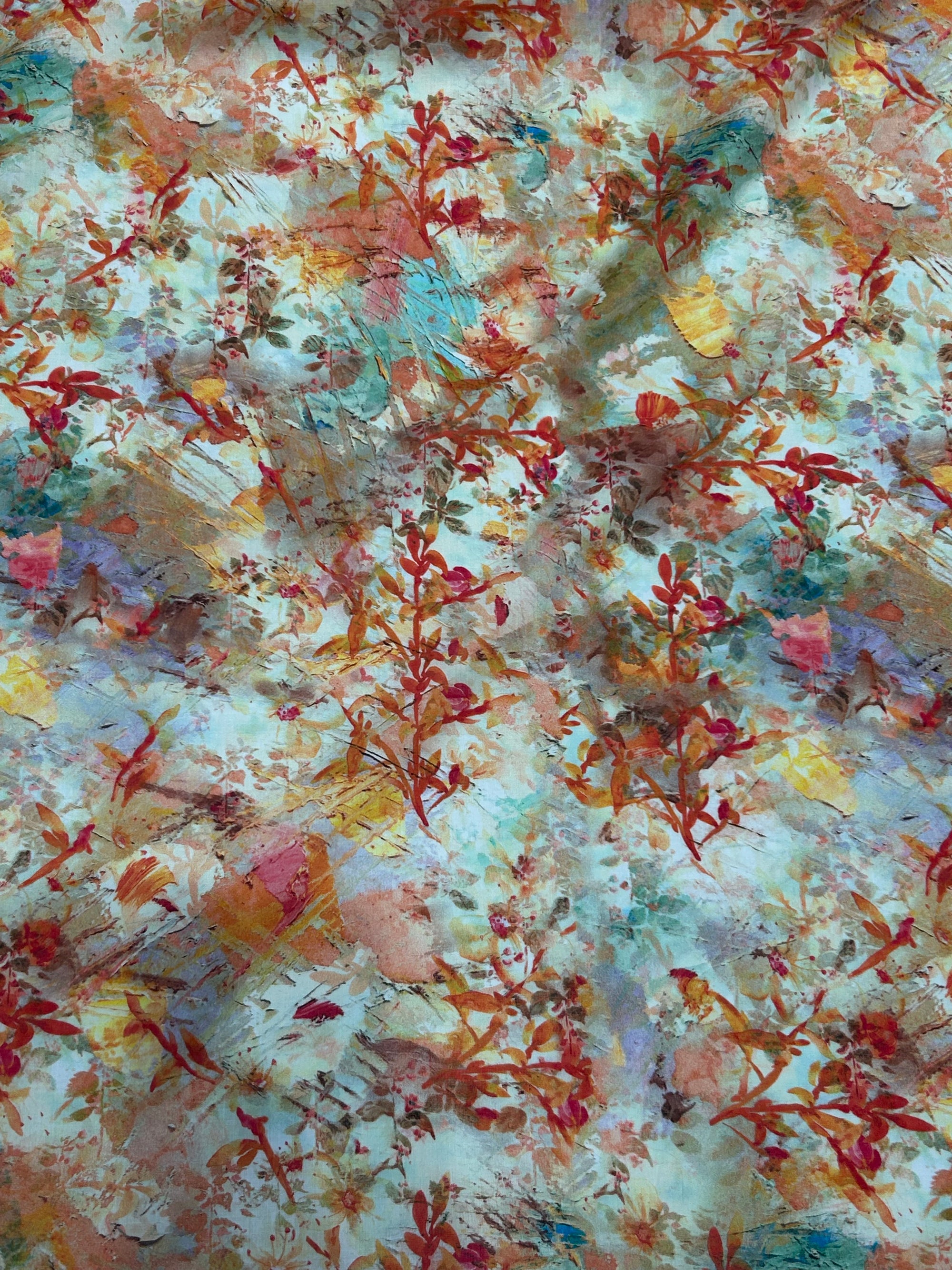 cotton lawn in a floral print with orange foliage and yellow, red, and blue paint brush strokes flat.