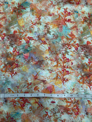 cotton lawn in a floral print with orange foliage and yellow, red, and blue paint brush strokes with measuring tape on top.
