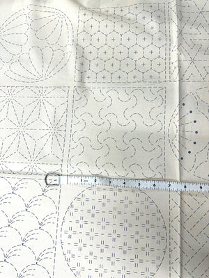 cream colored fabric with sashiko design squares printed on it with a measuring tape on top