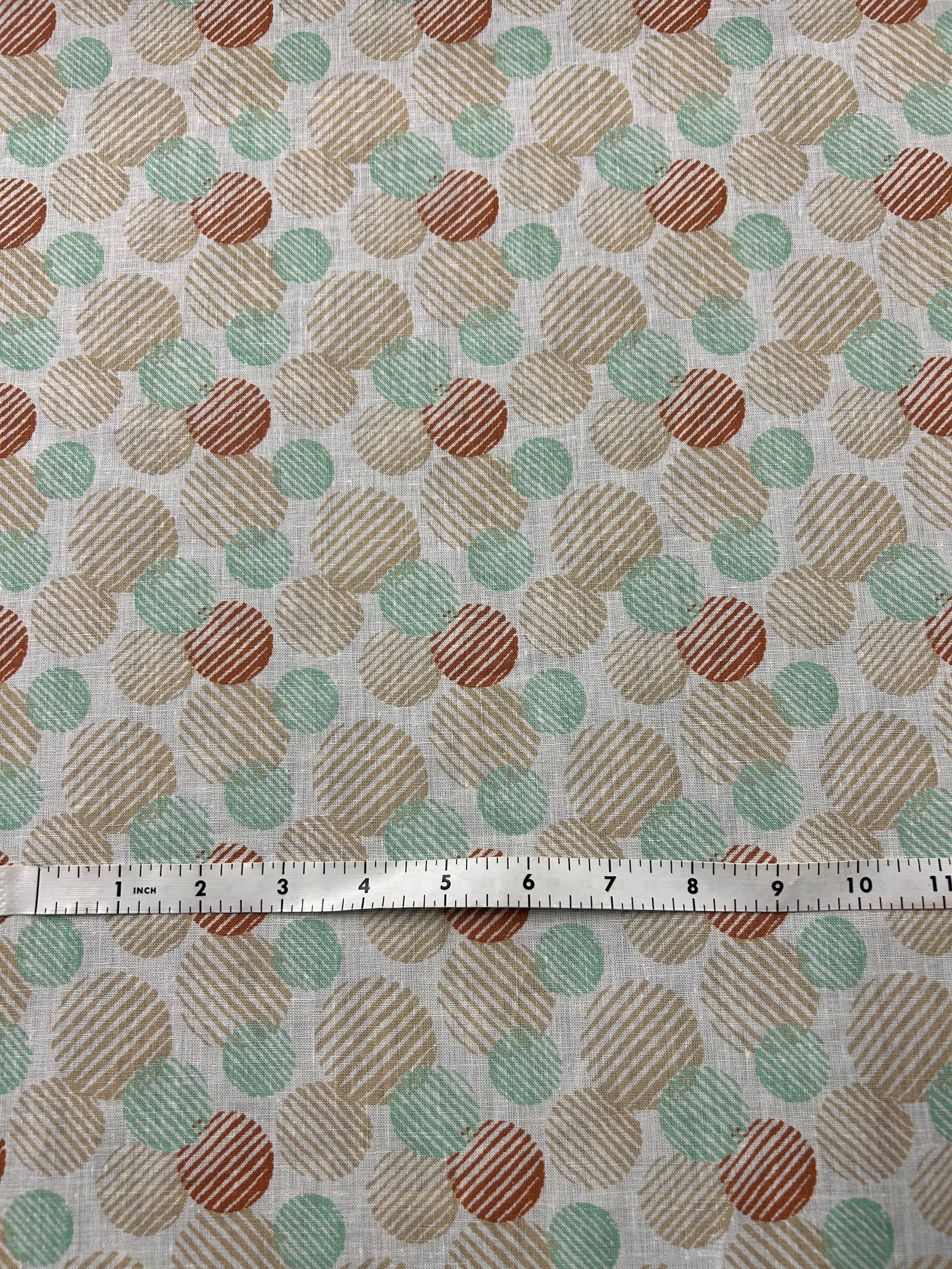 Linen fabric with a a retro abstract polka dot print fabric in mint, beige, and rust on an ivory background. The circles vary in size and are filled with fine diagonal stripe textures, creating a layered geometric look with a hand-printed feel.