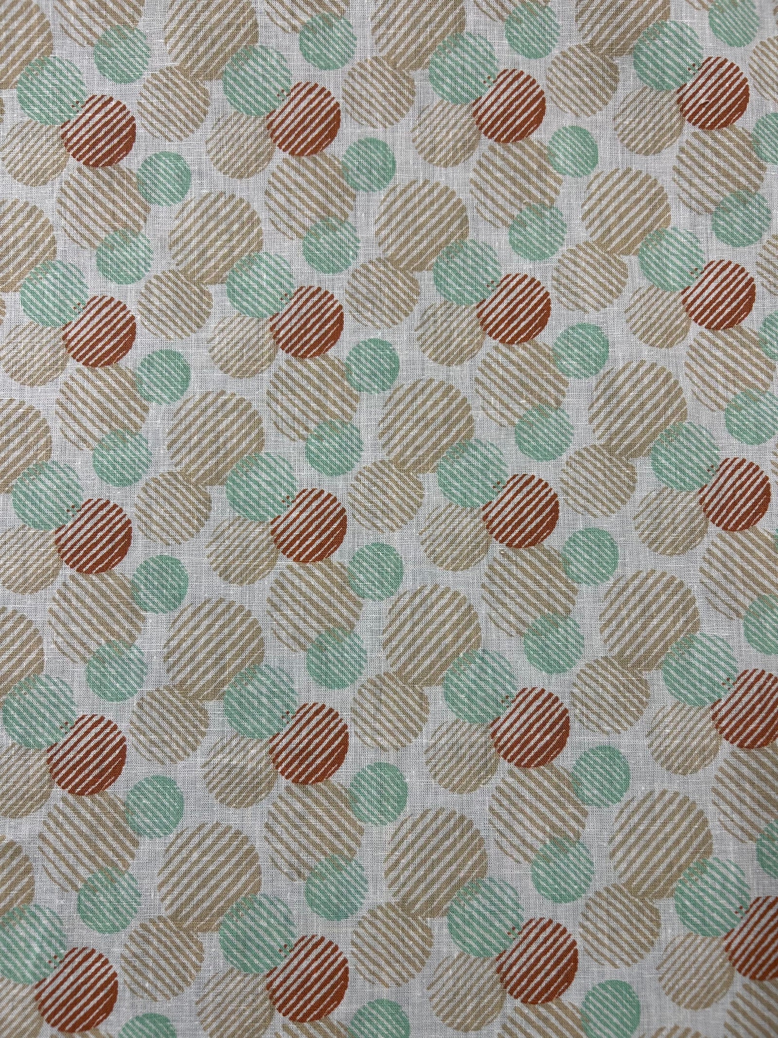 Linen fabric with a a retro abstract polka dot print fabric in mint, beige, and rust on an ivory background. The circles vary in size and are filled with fine diagonal stripe textures, creating a layered geometric look with a hand-printed feel.