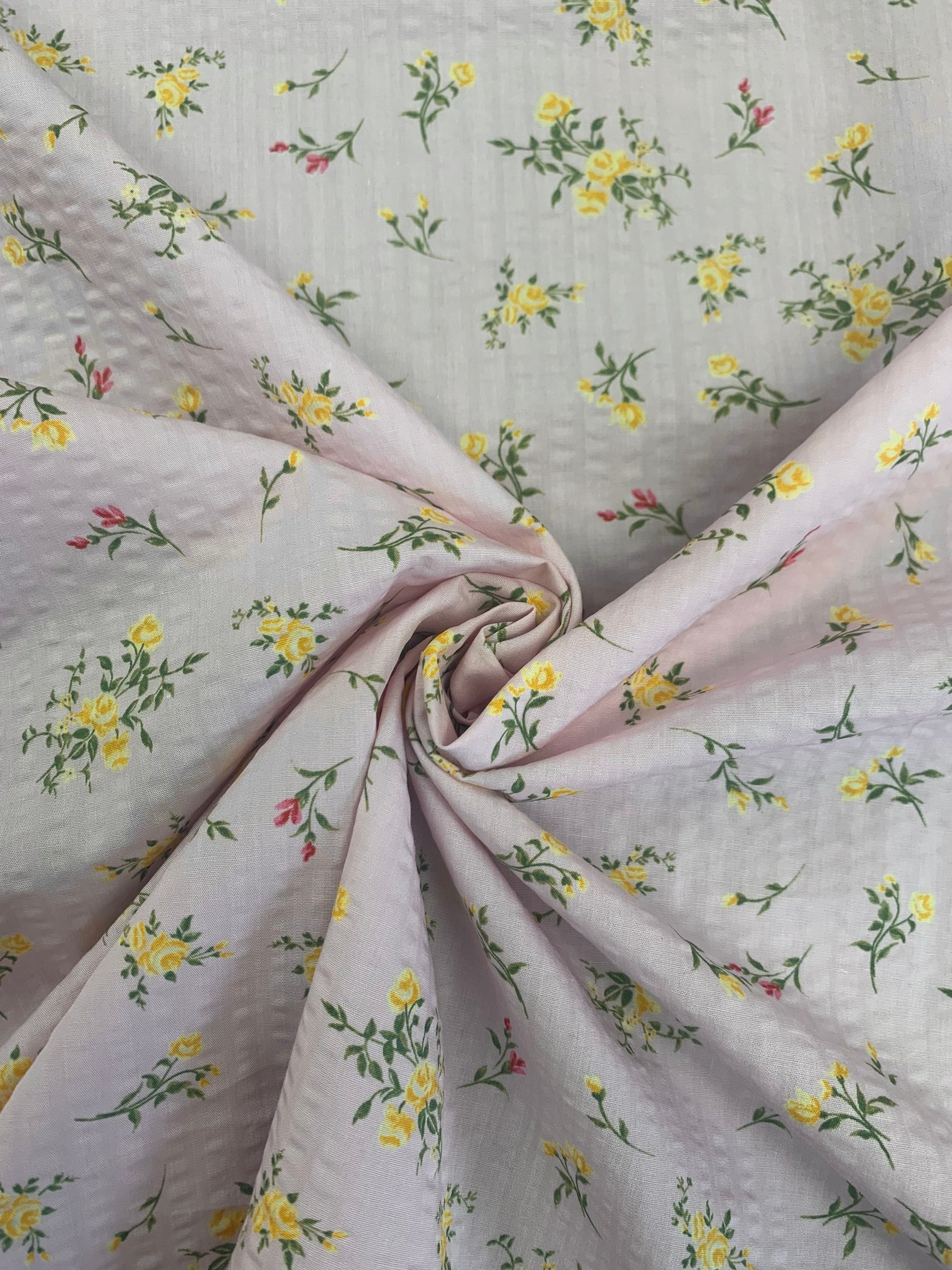 spiral close up of  pale pink lightweight flat cotton seersucker with a ditsy yellow floral print fabric.