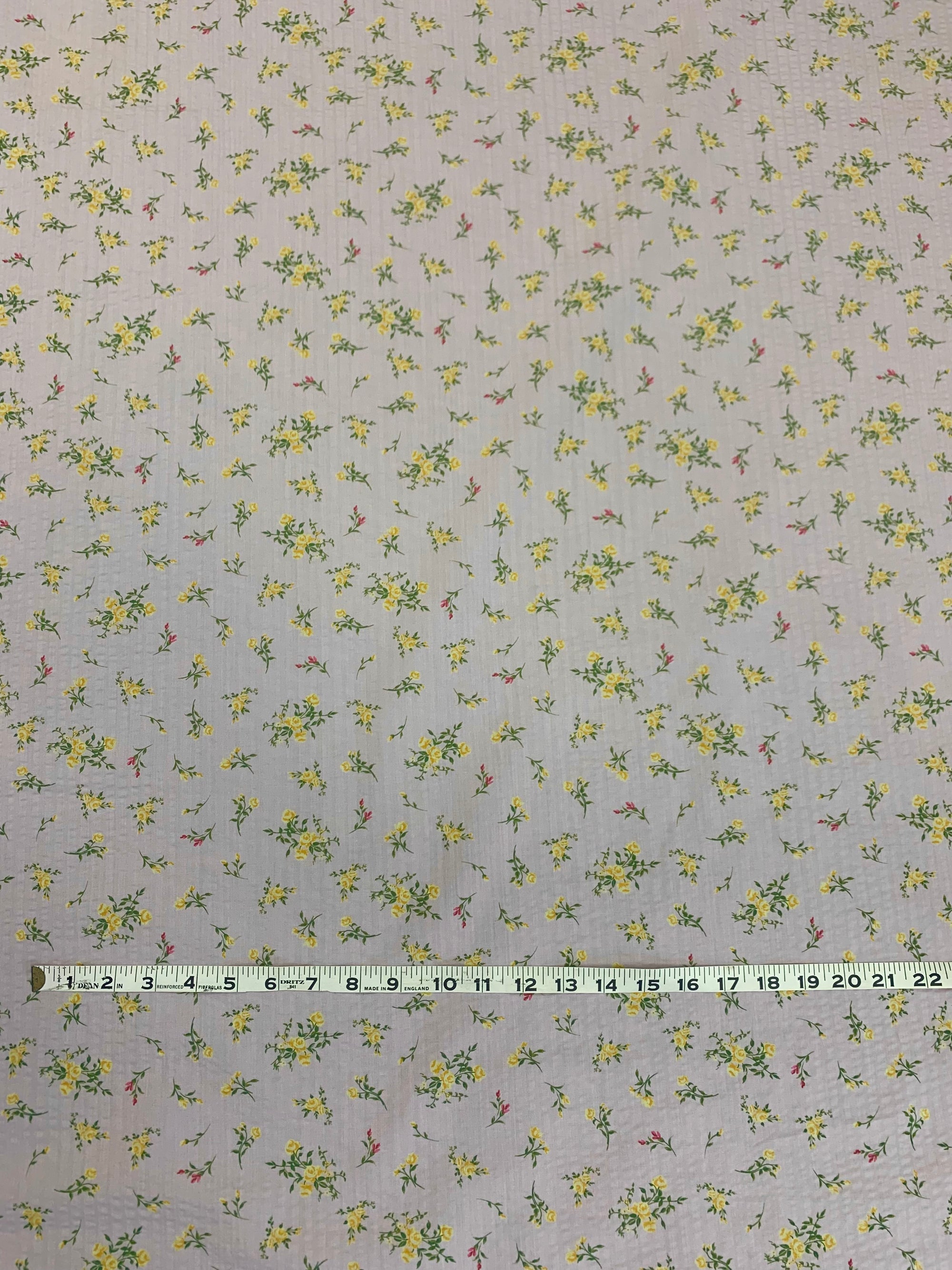  pale pink lightweight flat cotton seersucker with a ditsy yellow floral print fabric with a white measuring tape on top