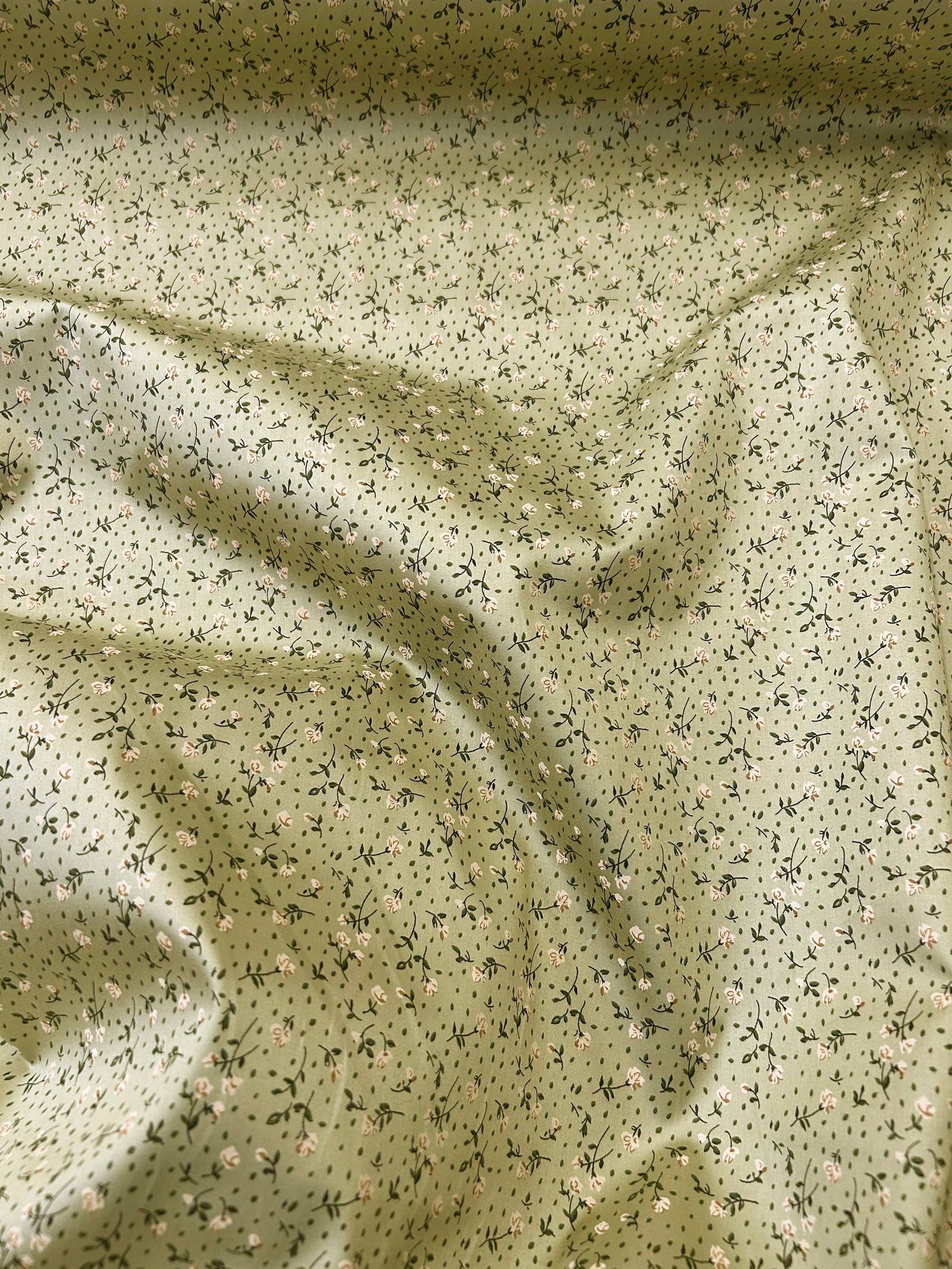 Draped ditsy pink floral print cotton fabric on a background of a light pastel bronzy green.
