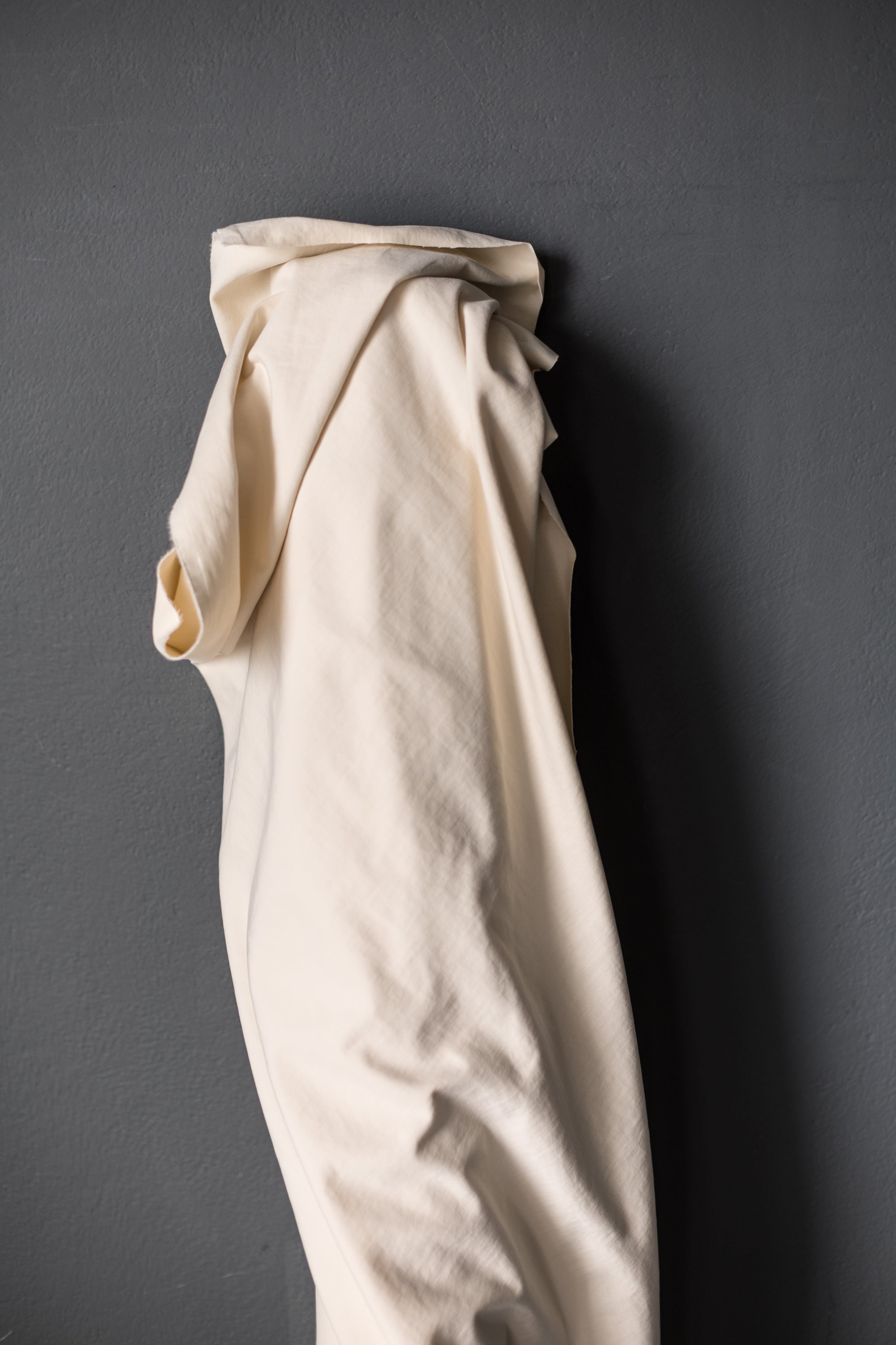 roll of ecru cotton sanded fabric displayed on a dark grey background.