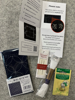 Embroidery kit components including fabric, needles, and tools on a gray surface