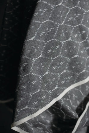 Close up of a  warp and weft of this ikat is in black and white threads which results in a soft grey colour with a white geometric pattern. On a dark grey background