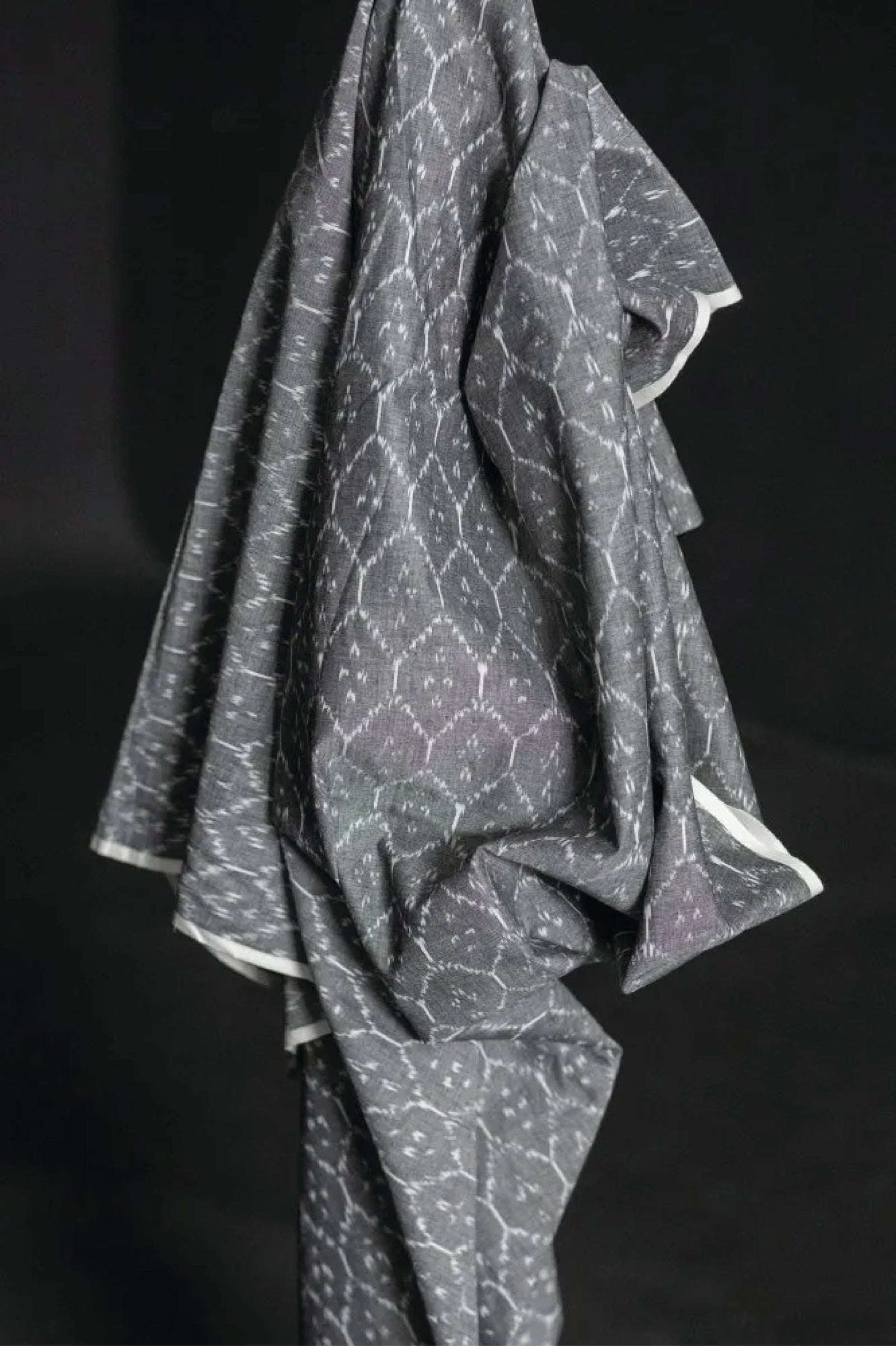 The warp and weft of this ikat is in black and white threads which results in a soft grey colour with a white geometric pattern. On a dark grey background