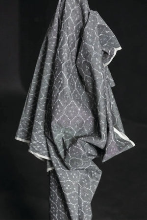 The warp and weft of this ikat is in black and white threads which results in a soft grey colour with a white geometric pattern. On a dark grey background