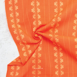 100% cotton fabric in a vibrant stunning orange color with a cream woven textured floral motif arranged in vertical rows in a swirl, on a white background.