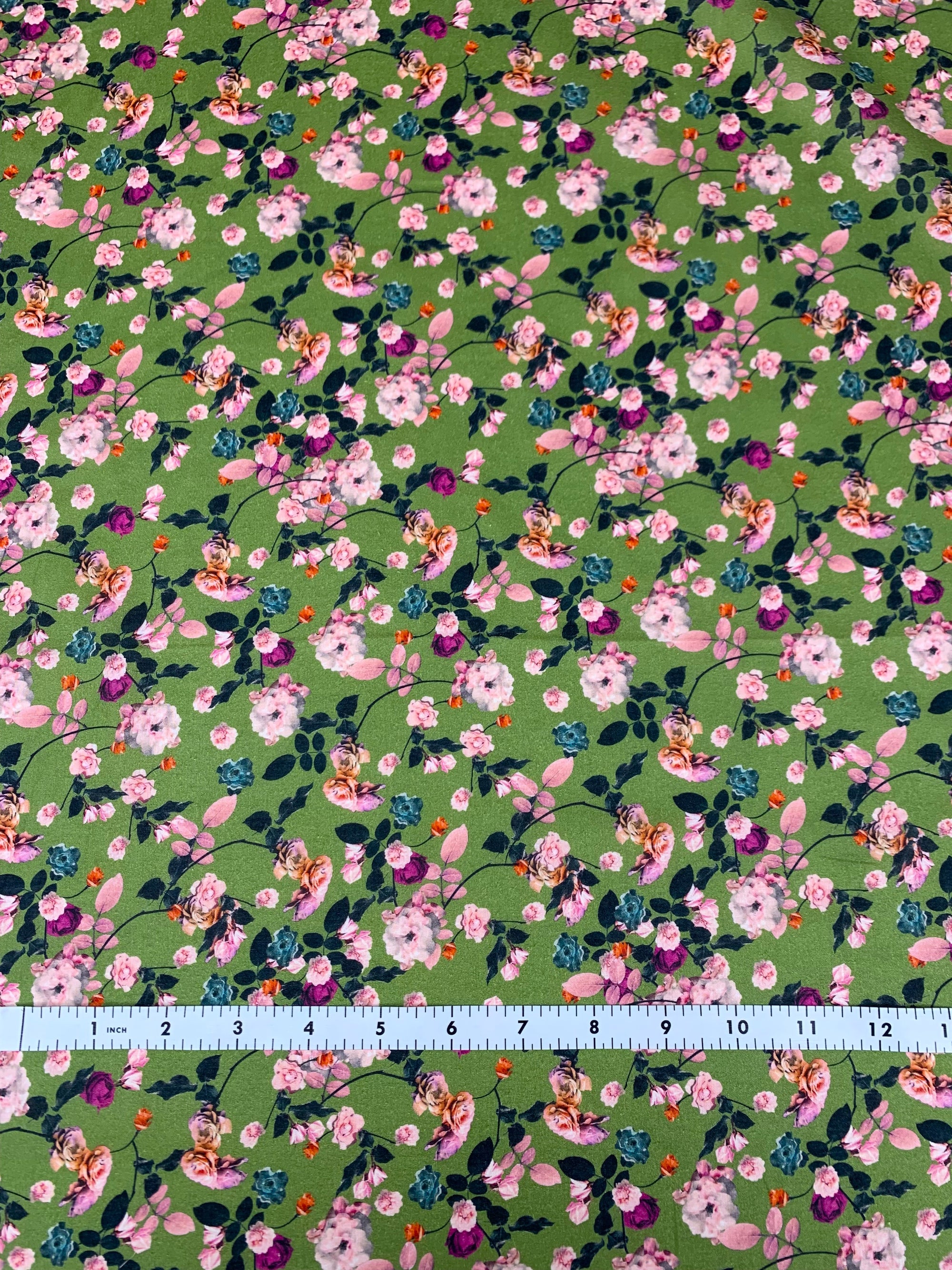 cotton lawn with pink and purple flowers  on a background of green.  With a measuring tape on the bottom of the fabric.
