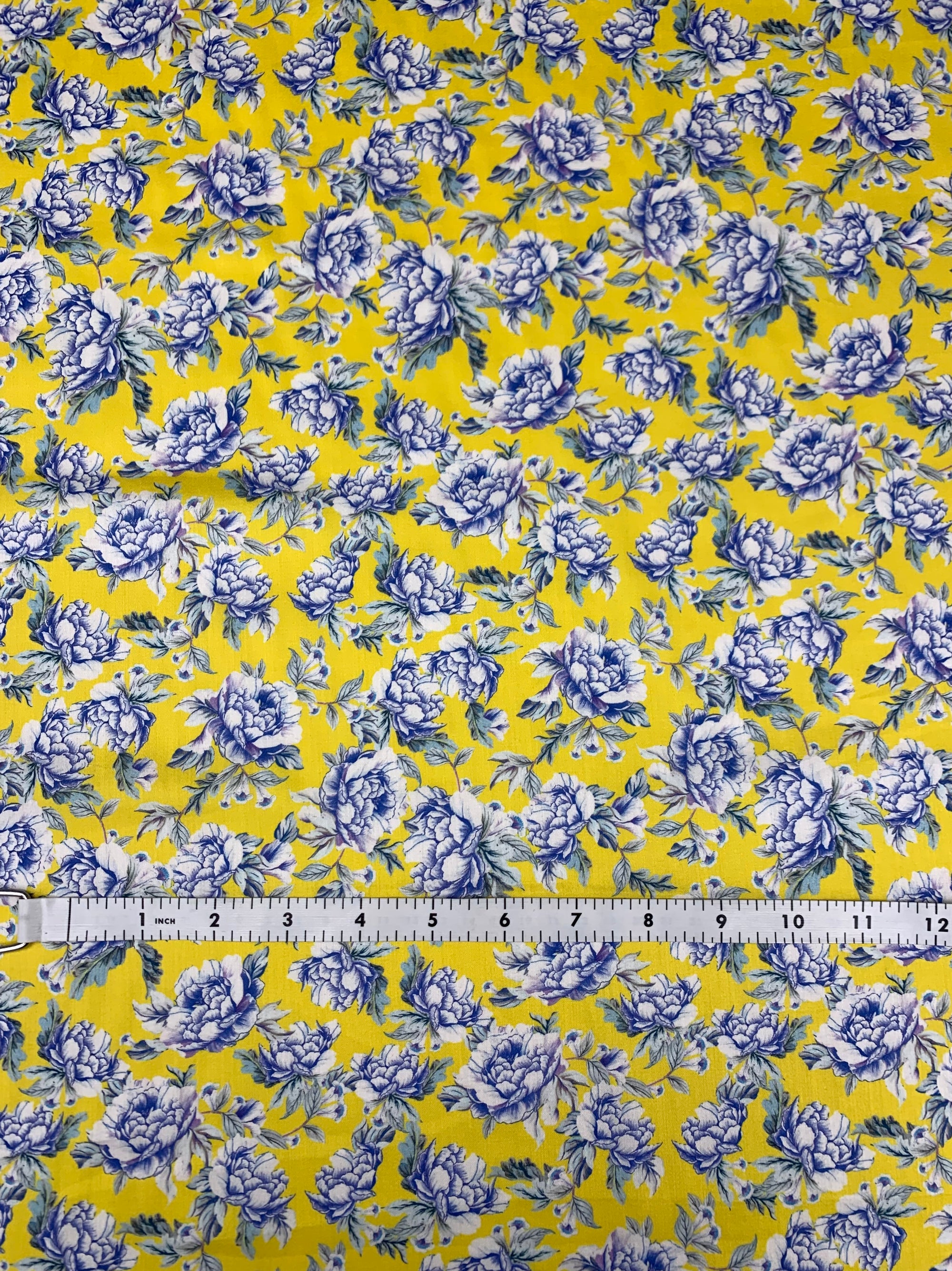 cotton lawn fabric with yellow and  blue/white flowers on a background of yellow with a measuring tape on the bottom