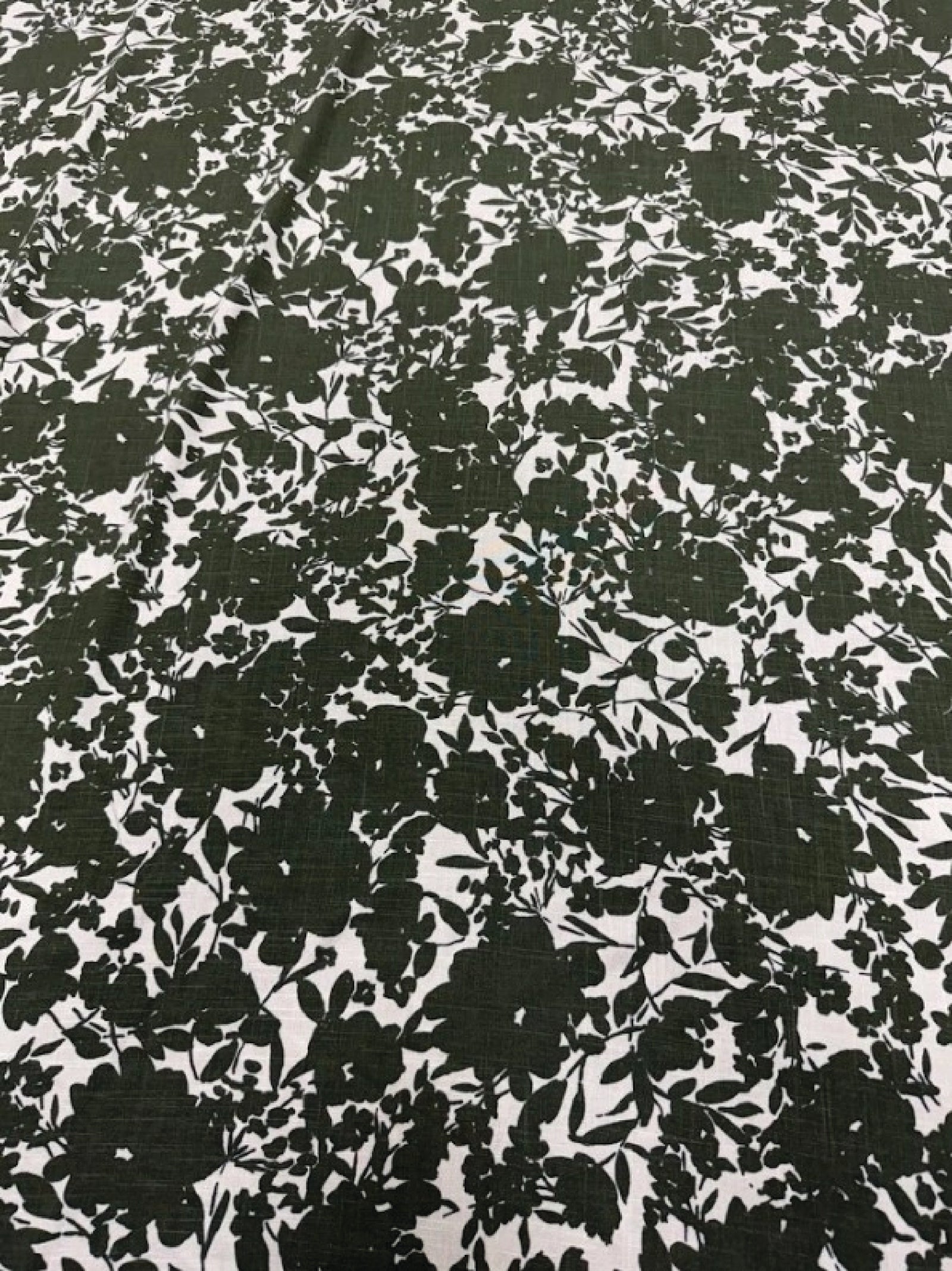 Close up of Italian linen with a green print of floral silhouettes on a white background.