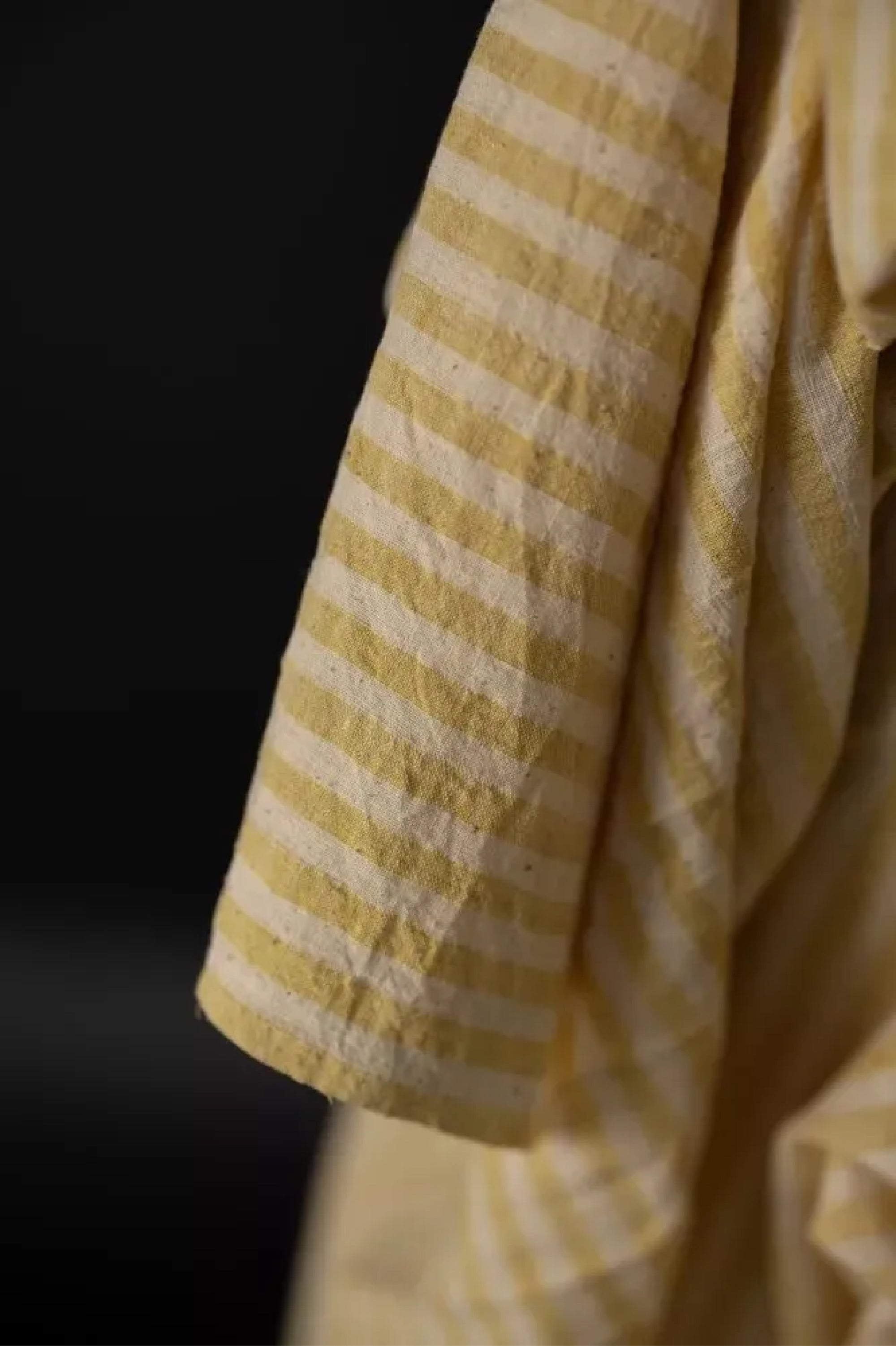 close up of a  handloomed sunshine stripe of warm yellow and natural with a loose weave and a washed out slubby texture on a dark grey background.