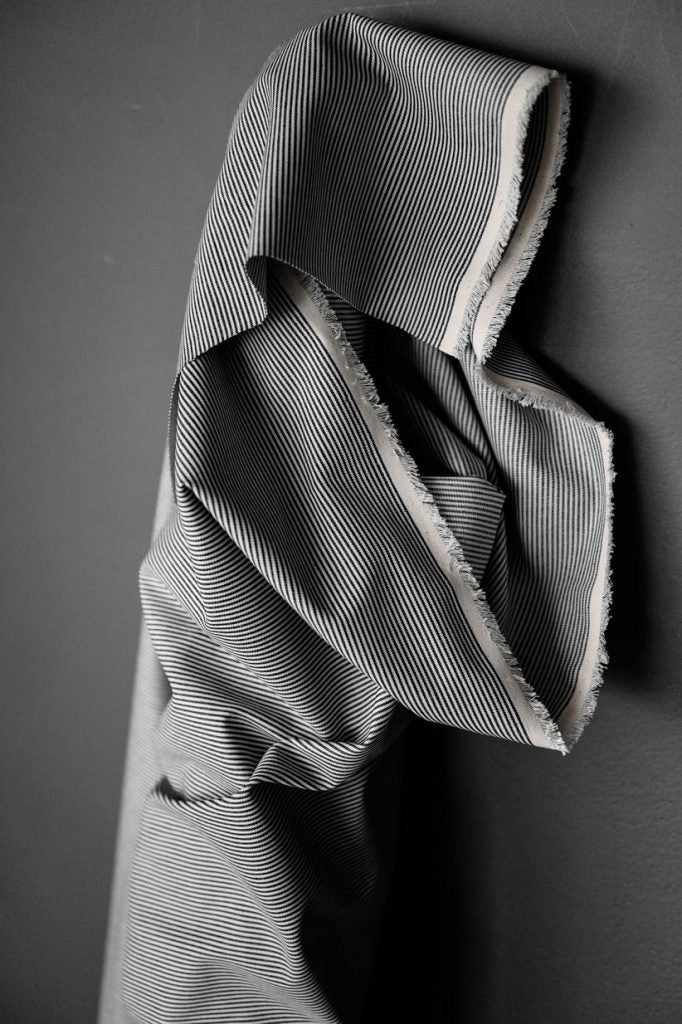 roll of dark navy and white skinny stripe cotton denim fabric standing up on a dark grey background.