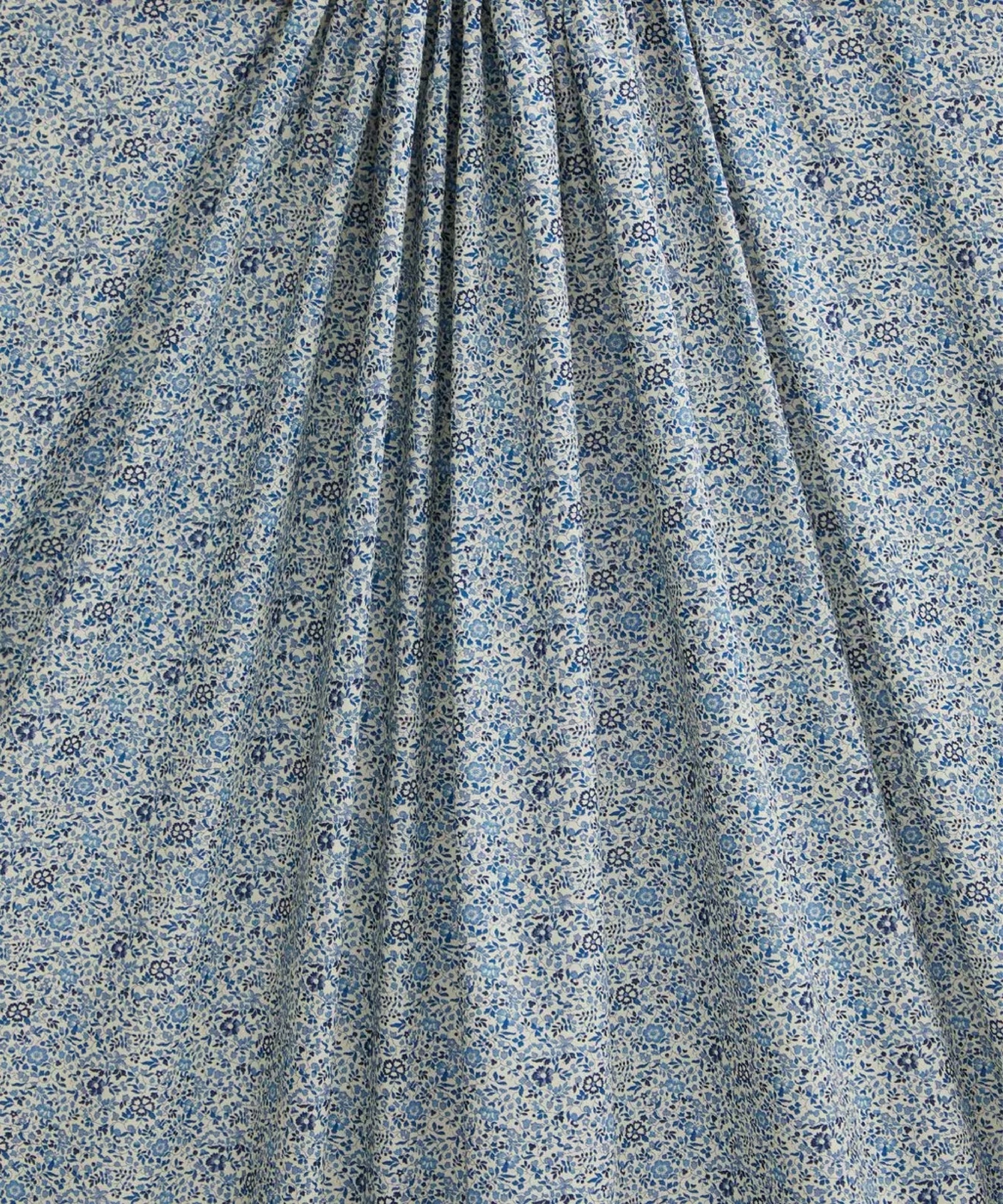 Close up of a cotton in a ditsy floral print with dainty blue flowers with a white background. A light brown ruler on top.